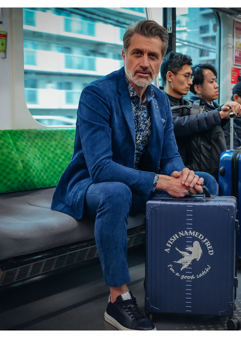 A Fish Named Fred Rib Broek Night Sky Blauw - Lifestyle: model zittend in de trein naast een koffer; broek en pasvorm zichtbaar.